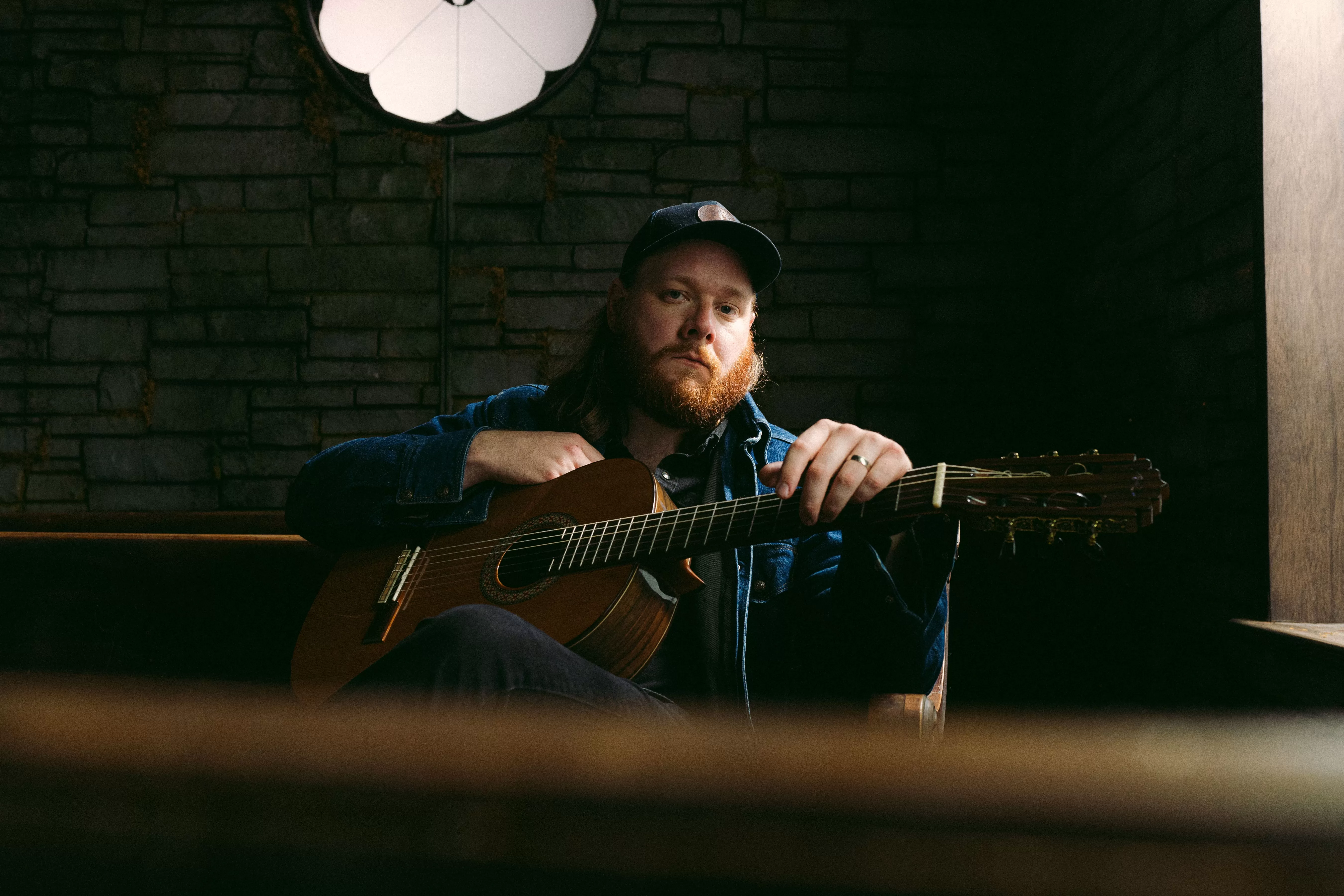 Photography light on brick wall, Mountain Thief in denim jacket plays guitar on wooden bench